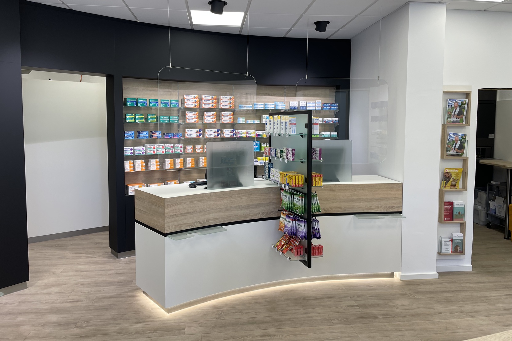 Moderne Apotheke mit Empfangstheke, Regalen voller Arzneimittel und informativen Brosch&uuml;ren an der Wand.