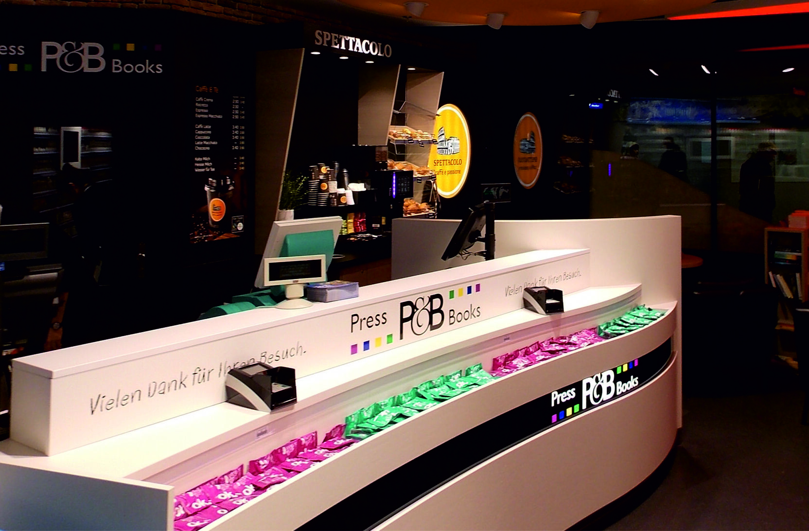 Moderne Verkaufsanordnung mit zwei Theken und farbiger Beleuchtung in einem Buchladen.