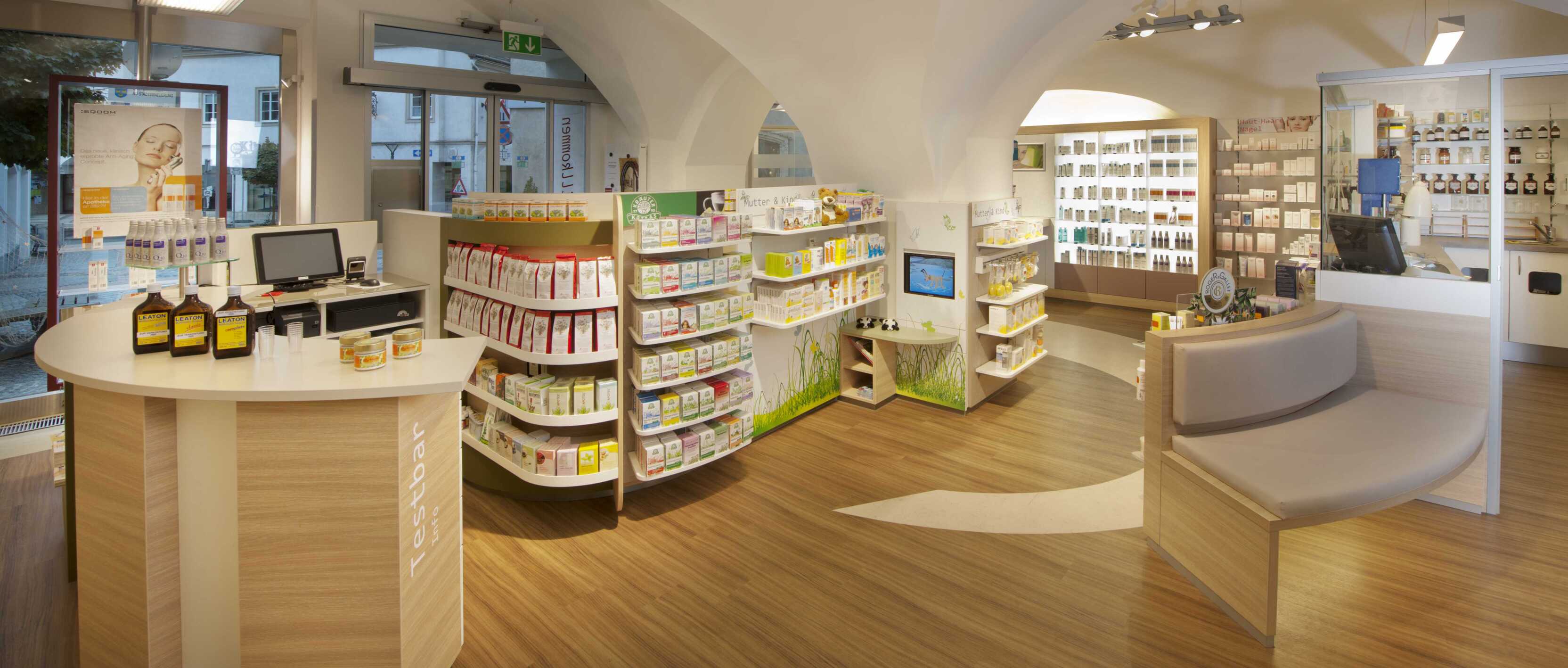 Innenansicht einer modernen Apotheke mit Regalen voller Produkte und einem Empfangstresen. Heller, einladender Raum.