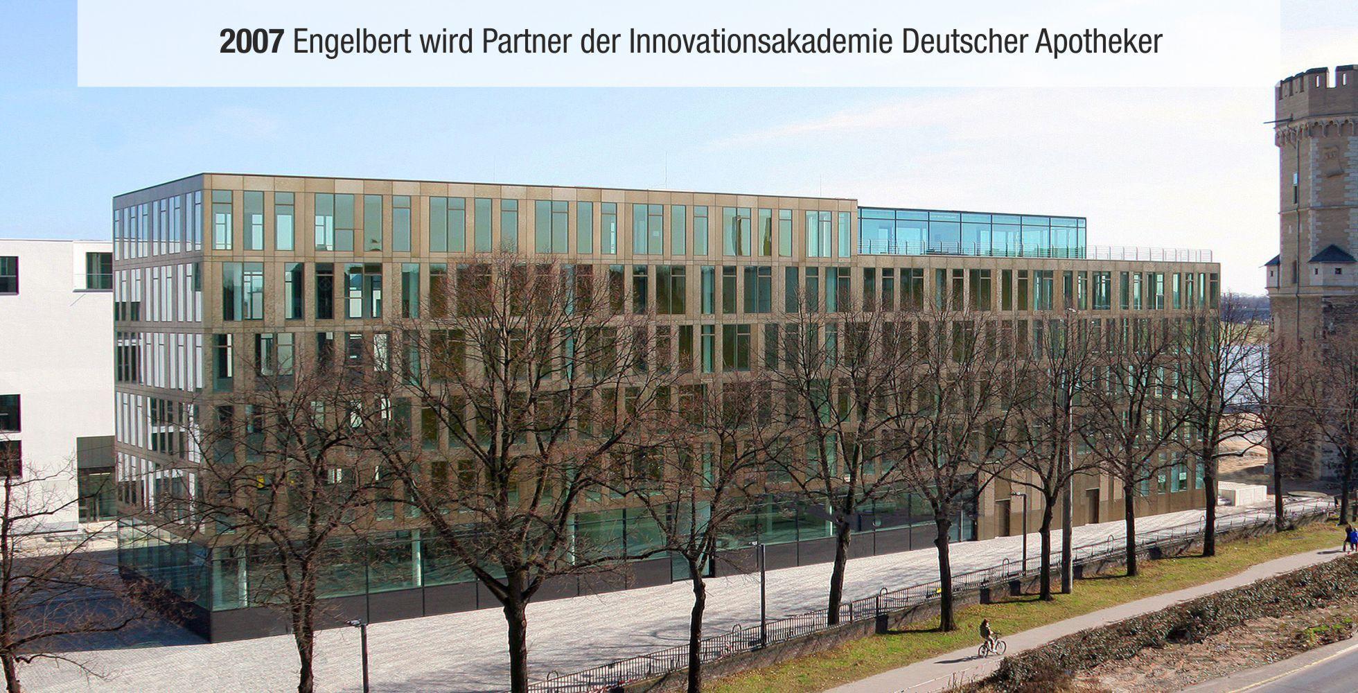 Moderne Geb&auml;ude mit Glasfront und Holzrahmen, umgeben von kahlen B&auml;umen und einem Gehweg.