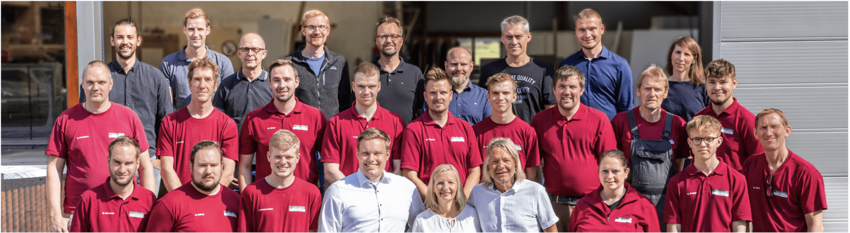 Gruppenfoto von 30 Personen in roten T-Shirts vor einem Geb&auml;ude, einige tragen Brillen, unterschiedliche Frisuren.