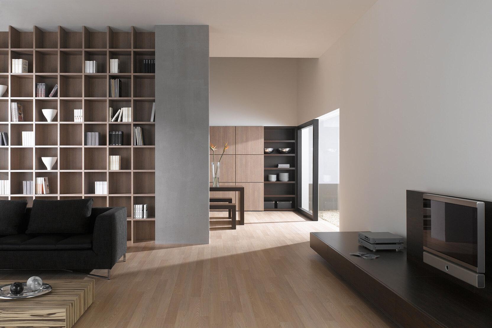 Offene Wohnraumimpression mit Einbauregal für Bücher und Dekoration in Trennwand mit hellem Holzboden