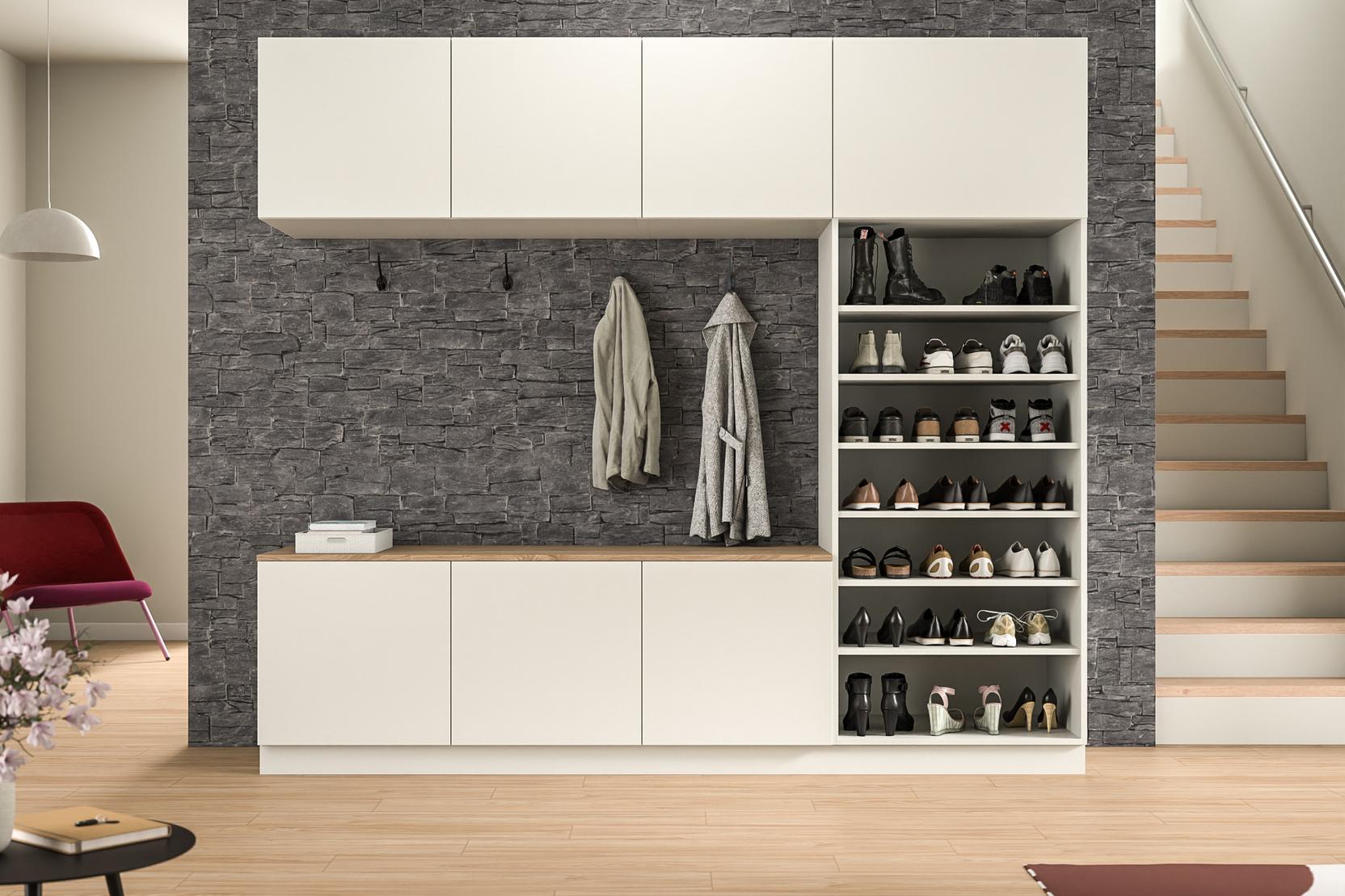 Maßgefertigter Schrankwand mit integrierter Garderobe im Eingangsbereich. Eine stilvolle Schrankwand nach Maß in weißer Farbe mit Schubfächern und einer offenen Nische für Jacken, vor einer markanten Steinwand, im Eingangsbereich.